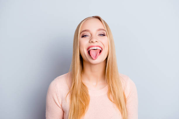 Close up portrait of funny childish playful careless carefree cheerful excited joyful beautiful delightful with long blond straight hairdo woman demonstrating tongue isolated on gray background Close up portrait of funny childish playful careless carefree cheerful excited joyful beautiful delightful with long blond straight hairdo woman demonstrating tongue isolated on gray background delightful stock pictures, royalty-free photos & images