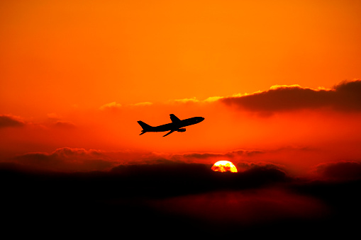 flying commercial airplane silhouetted by sunset.
