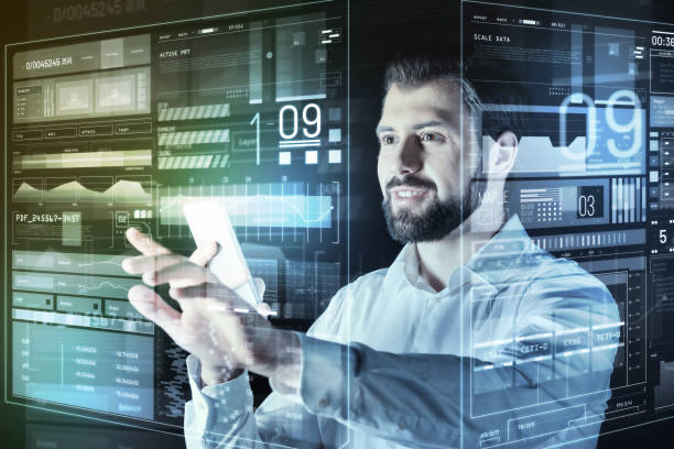 istock Handsome programmer holding a smartphone and looking at the screen of computer 935351282