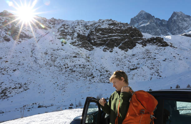 istock Young man throws on backpack by car parked in mountains 935356134