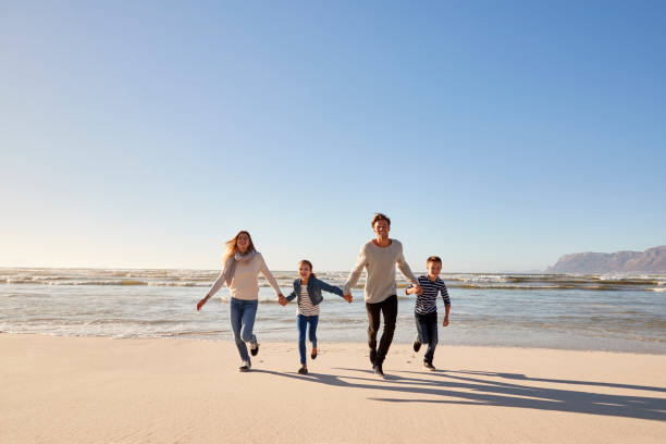 istock Family On Winter Beach Holding Hands And Running Towards Camera 935359914