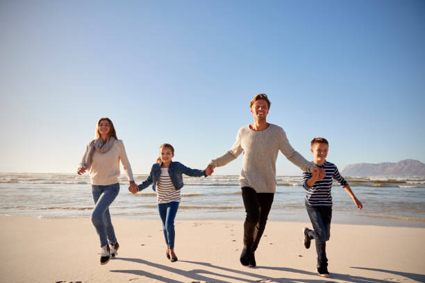 istock Family On Winter Beach Holding Hands And Running Towards Camera 935360008