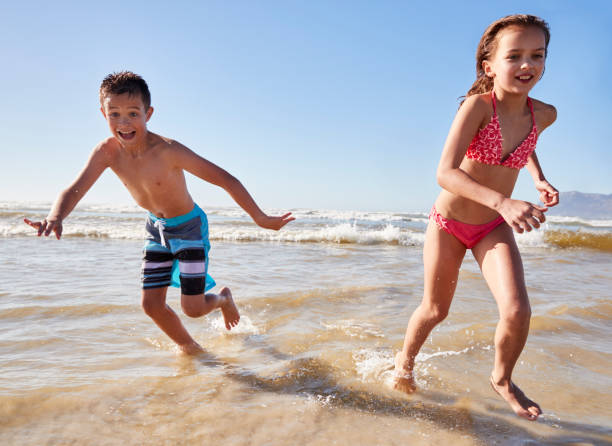 istock Boy And Girl On Summer Vacation Running Through Waves 935360244