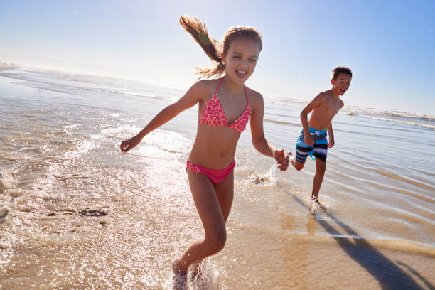 istock Boy And Girl On Summer Vacation Running Through Waves 935360246