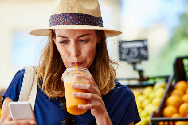 mujer beber jugo mientras esté usando el teléfono en la tienda - drinking straw drinking juice women fotografías e imágenes de stock