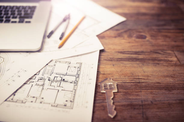 Turnkey projects Transparent house-shaped key on wooden desk beside architectural blueprints of apartment building project turnkey project stock pictures, royalty-free photos & images