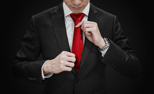 Businessman in black suit tying red necktie on black background