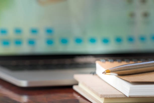 istock Closeup pen and notebook with blurry laptop background 935389642