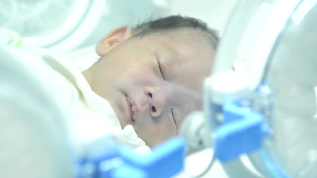 Close up of newborn baby inside incubator, portrait of young asian newborn baby boy sleeping inside medical intensive care units incubator at hospital.