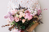 Florist woman holding a beautiful fresh blossoming flower bouquet of peony, roses, lilac, eustoma, mattiola in pink and lavender colors on the grey wall background