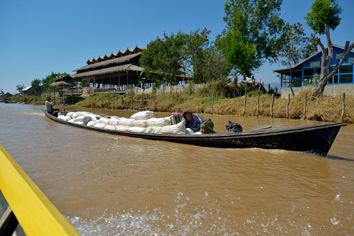 LAKE INLE, MYANMAR - FEBRUARY 27, 2015: Burmese workers transporting by wooden, long boat a freight. This kind of transportation is typical for Lake Inle, Myanmar.