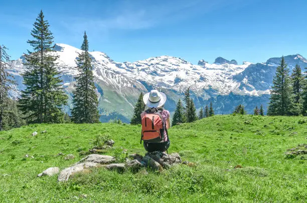 Swiss Alps. A woman in a white hat is sitting on a green meadow, admiring the mountain scenery. Engelberg Resort