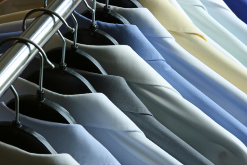 Close-up of many dry cleaned and ironed men's shirts in different colors on hangers hanging on a metal rack. Could also be laundry or shirts at a clothing store. Top partial view.