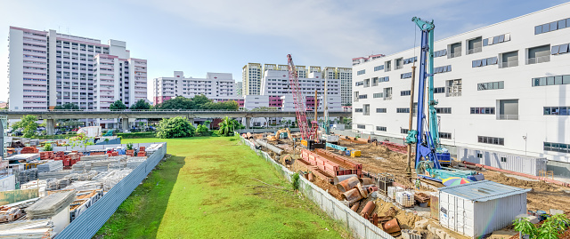Panorama construction site near completed HDB complex, MRT station at Eunos, Singapore. Foundation, ground works in progress. Heavy machinery, pile driver, building material, scaffolding, fence