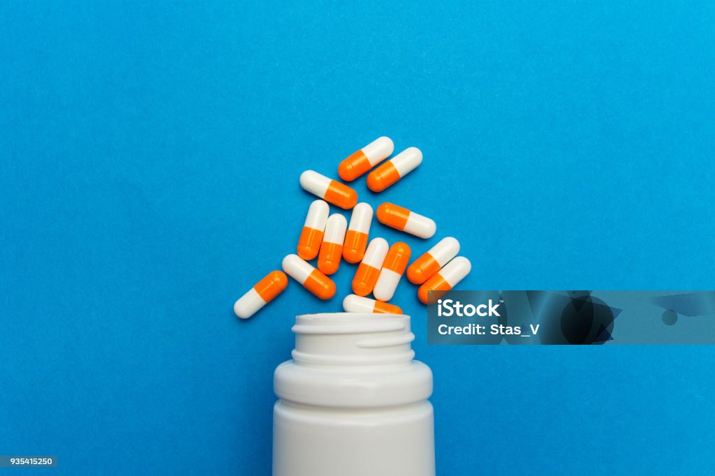 Orange white capsules (pills) were poured from a white bottle on a blue background. Medical background, template. Capsule - Medicine Stock Photo