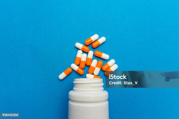 Orange White Capsules Were Poured From A White Bottle On A Blue Background Medical Background Template Stock Photo - Download Image Now