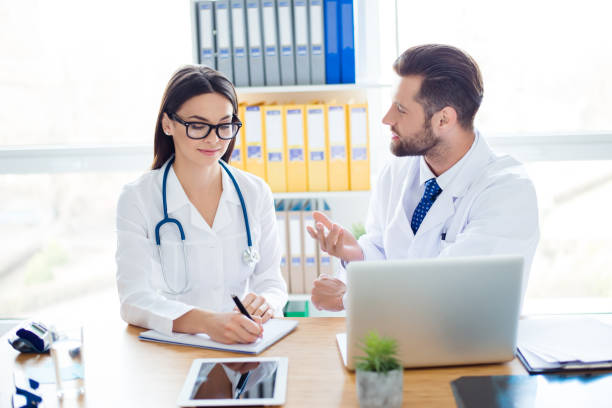 istock Team building concept. Two medic workers in white coats are discussing the diagnosis and make notes of prescription. Workstation is so modern and light 935422094