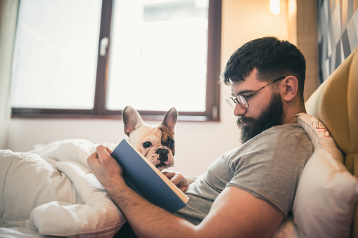 Man reading book in the bed, cuddling with his dog