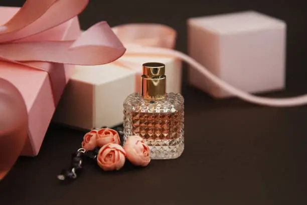 Photo of Women's Pink Perfume in Beautiful Bottle and Artificialt Flowers Bracelet on Brown Background with gift boxes on Background.