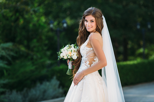 Impresionante novia hermosa boda blanco vestido espera bouquet de flores en sus manos. Concepto de ropa y florística photo