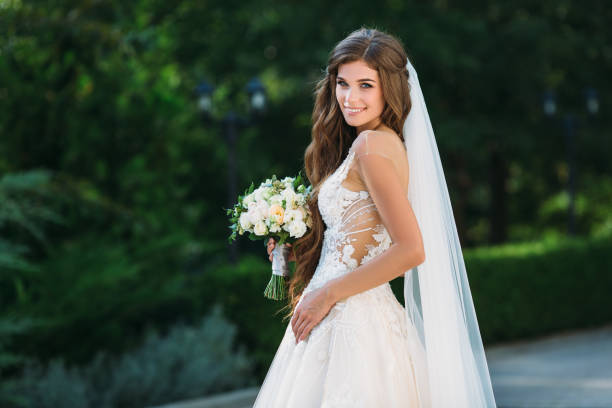 incredibile sposa in bellissimo abito da sposa bianco tenere bouquet di fiori tra le mani. concetto di abbigliamento e fioristica - hairstyle love wedding photography foto e immagini stock