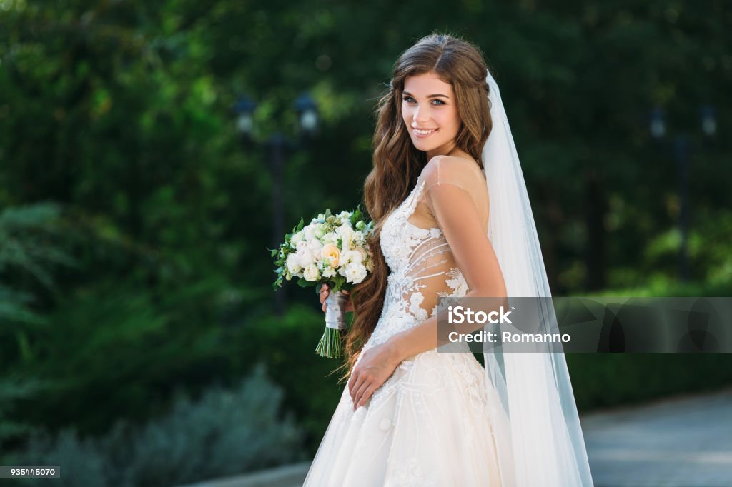 Amazing bride in beautiful white wedding dress hold bouquet of flowers in her hands. Concept of clothes and floristics Amazing bride in beautiful white wedding dress hold bouquet of flowers in her hands. Concept of clothes and floristics. Bride Stock Photo