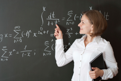 Portrait of a beautiful young businesswoman wearing a white shirt and a skirt and thinking. She is looking upwards. A blackboard with formulas on it