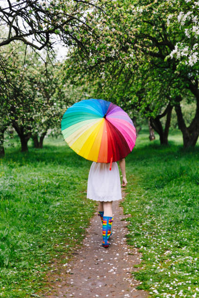 mädchen in einem weißen kleid im blühenden garten mit bunten regenbogen-regenschirm spazieren. frühling im freien. - apple blossom single flower spring blossom stock-fotos und bilder