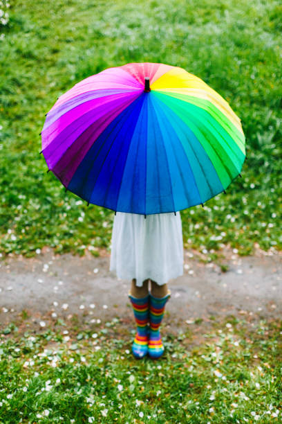 カラフルな虹傘を借りて咲く庭に立っている白いドレスの女の子。春、屋外。 - wet dress rain clothing ストックフォトと画像