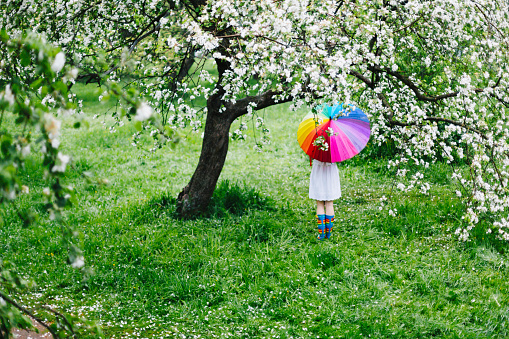 Girl in colorful rain boots in the blooming garden. Spring weather concept.