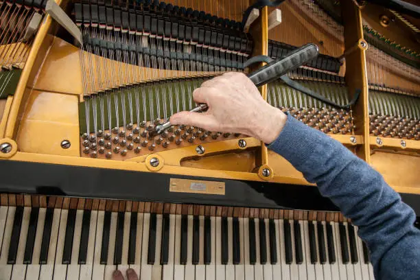 Photo of hand and tools of tuner working on grand piano