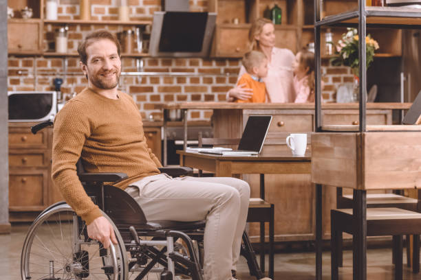 istock disabled middle aged man in wheelchair smiling at camera while spending time with family at home 935475754