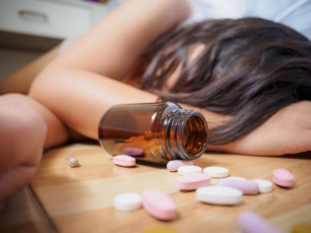 young woman is lying on the floor with a lot of pills. overdose and suicide concept. - alcoholism narcotic excess alcohol imagens e fotografias de stock