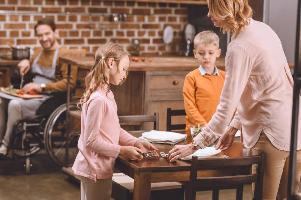 istock siblings with mother serving table for dinner while disabled father in wheelchair cutting vegetables behind 935480600