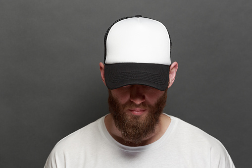Hermoso modelo masculino hipster con barba con camiseta blanca en blanco y una gorra de béisbol con espacio para su logo o diseño en estilo casual urbano photo