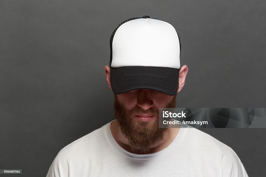 Hipster handsome male model with beard wearing white blank t-shirt and a baseball cap with space for your logo or design in casual urban style Baseball Cap Stock Photo