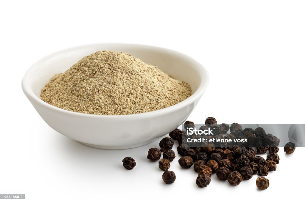 Finely ground white pepper in white ceramic bowl next to black peppercorns isolated on white. Bowl Stock Photo