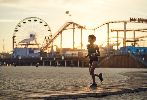 athletic african american woman jogging on boardwalk at sunset on beach