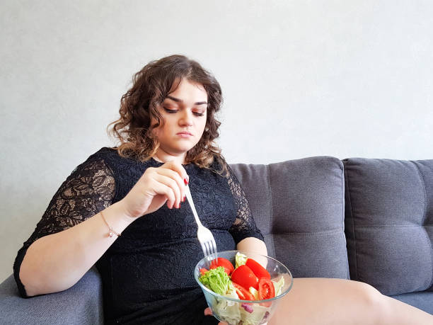 triste menina completa com salada no sofá - overweight women salad frustration - fotografias e filmes do acervo