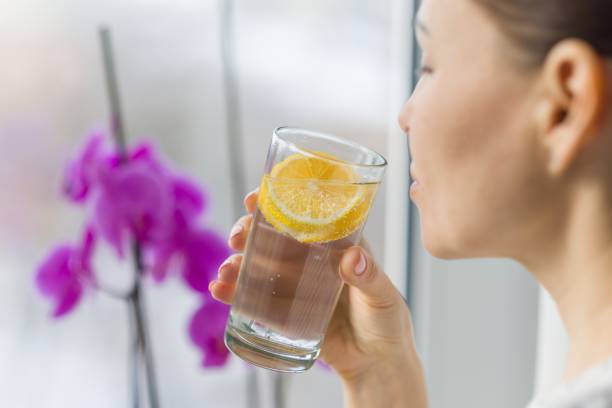 Woman drinking summer refreshing fruit flavored infused water with fresh organic lemon. stock photo