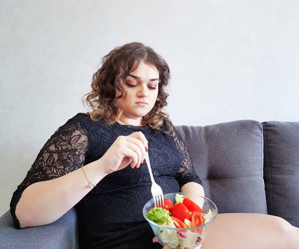 triste fille complet avec salade sur le canapé - overweight women salad frustration photos et images de collection