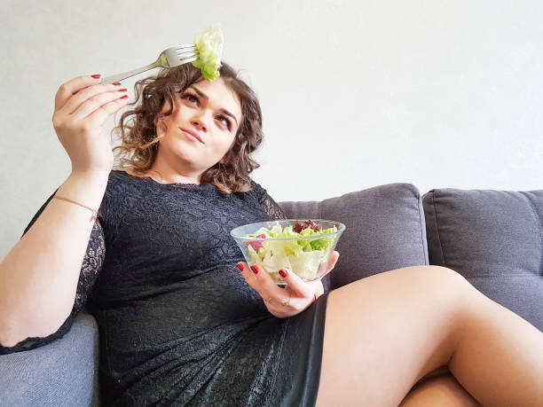 triste menina completa com salada no sofá - overweight women salad frustration - fotografias e filmes do acervo