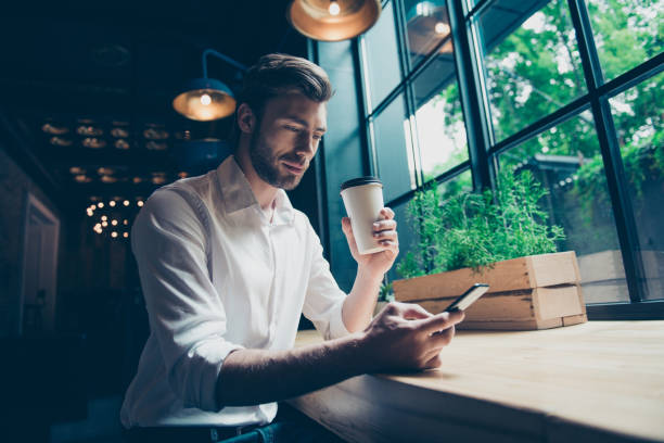 istock Low angle view of a handsome brunet guy entrepreneur having a coffee break in a loft styled restaurant, looking serious, well dressed, with phone and tea 935506982