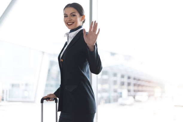 istock attractive young stewardess with suitcase waving at camera in airport 935512610