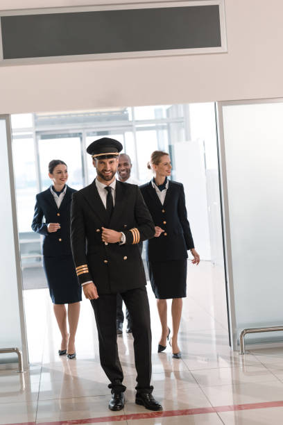 handsome young pilot walking by airport with his team - cabin crew pilot airport walking imagens e fotografias de stock