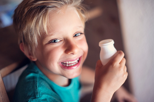 Cute laughing little boy enjoys a little bottle of yogurt. The boy aged 7 is smiling at the camera.
Nikon D800