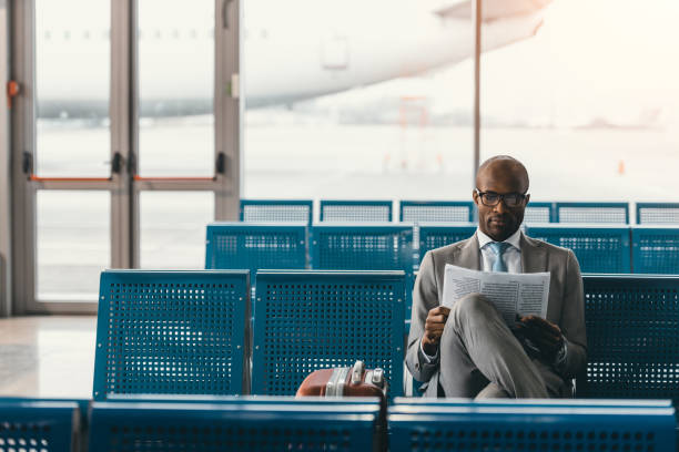 serious businessman reading newspaper waiting for flight at airport lobby serious businessman reading newspaper waiting for flight at airport lobby newspaper airport reading business person stock pictures, royalty-free photos & images