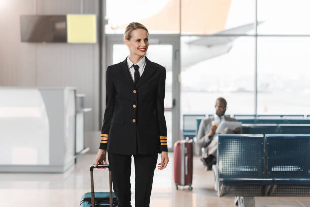 女性パイロットを浮かべて歩いて空港のロビーでスーツケース - cabin crew pilot airport walking ストックフォトと画像