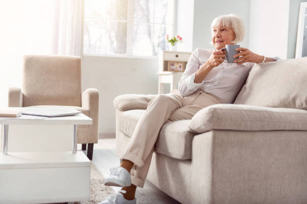 Petite elderly woman drinking coffee in her living room