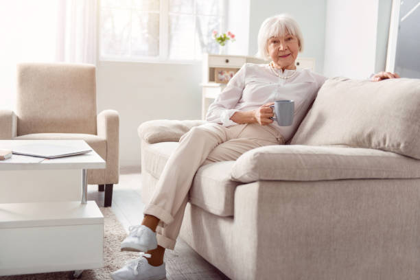 istock Charming elderly lady relaxing with coffee cup on couch 935567256